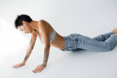 sensual tattooed woman in satin bra and blue jeans posing on grey background Stickers #638592902