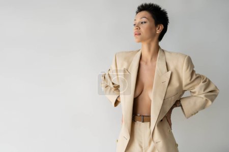 Photo for Young woman in beige suit on sexy shirtless body standing with hands on waist isolated on grey - Royalty Free Image