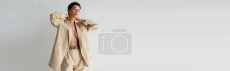 Photo for Sexy woman wearing oversize suit on shirtless body and looking at camera isolated on grey, banner - Royalty Free Image
