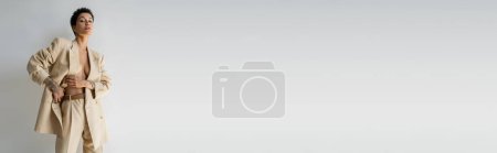 Photo for Sexy brunette woman wearing stylish suit on shirtless body and looking at camera isolated on grey, banner - Royalty Free Image