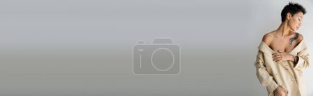 Téléchargez les photos : Femme tatouée sexy posant avec des épaules nues et blazer beige sur fond gris, bannière - en image libre de droit