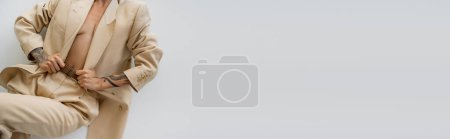 Photo for Partial view of sexy tattooed woman in beige suit on shirtless body posing on grey background, banner - Royalty Free Image