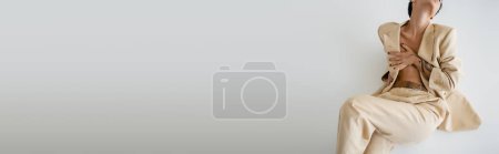 Téléchargez les photos : Vue recadrée de femme torse nu en costume élégant couvrant la poitrine avec la main sur fond gris, bannière - en image libre de droit