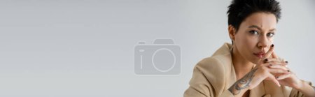 Téléchargez les photos : Portrait of serious brunette woman with clenched hands looking at camera isolated on grey, banner - en image libre de droit