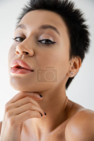 Nahaufnahme Porträt einer jungen Frau mit kurzen brünetten Haaren und Make-up, die in die Kamera schaut, isoliert auf grau