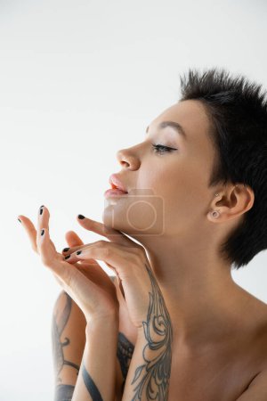 Téléchargez les photos : Portrait of tattooed brunette woman with makeup looking away isolated on grey - en image libre de droit