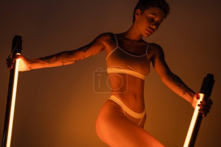 sexy mujer joven en lencería de pie con lámparas fluorescentes brillantes sobre fondo oscuro