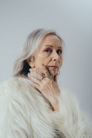 Porträt einer Seniorin mit Ringen an den Fingern, die isoliert auf graue Kamera blickt  