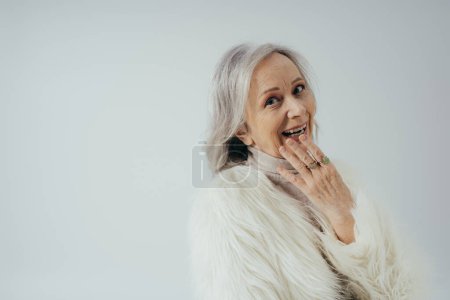 retrato de mujer mayor feliz con anillos en los dedos mirando a la cámara aislada en gris 
