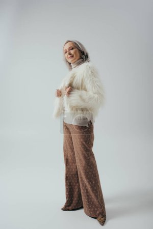 Foto de Longitud completa de la mujer mayor en chaqueta de piel sintética posando sobre fondo gris - Imagen libre de derechos