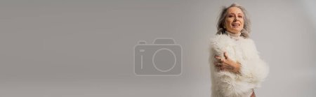 Téléchargez les photos : Heureuse femme âgée en fausse fourrure blanche regardant caméra sur gris, bannière - en image libre de droit