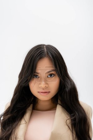 Téléchargez les photos : Portrait de jolie femme asiatique avec de longs cheveux bruns et maquillage naturel regardant caméra isolée sur gris - en image libre de droit