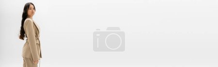 Téléchargez les photos : Femme asiatique avec de longs cheveux bruns debout en veste beige isolé sur gris, bannière - en image libre de droit