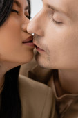 close up view of man with closed eyes kissing charming asian woman isolated on grey hoodie #640565108