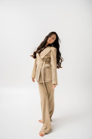 Photo for Full length of barefoot woman with long hair posing in fashionable pantsuit on grey background - Royalty Free Image