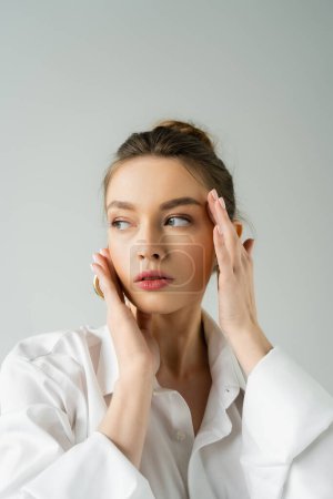 Photo for Portrait of pretty young woman with natural makeup and hands near face looking away isolated on grey - Royalty Free Image