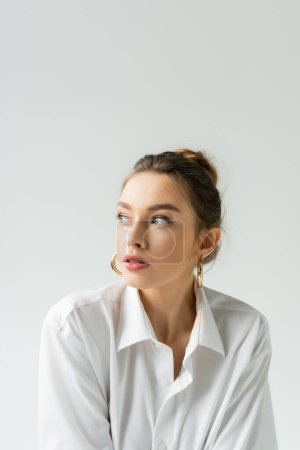 Photo for Portrait of young woman in white shirt and hoop earrings looking away isolated on grey - Royalty Free Image
