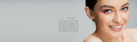 Téléchargez les photos : Portrait of happy young woman with makeup smiling at camera isolated on grey, banner - en image libre de droit