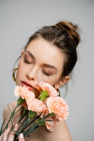 Photo for Portrait of young sensual woman posing with closed eyes near bouquet of peach carnations isolated on grey - Royalty Free Image