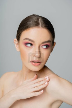 Photo for Pretty woman with makeup touching perfect skin on naked shoulder while looking away isolated on grey - Royalty Free Image