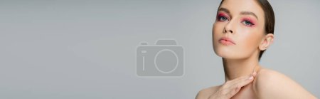 Photo for Sensual woman with makeup looking at camera and touching naked shoulder isolated on grey, banner - Royalty Free Image