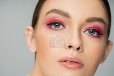 Nahaufnahme Porträt einer jungen Frau mit rosa Make-up, die isoliert auf grau in die Kamera blickt