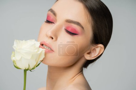 Photo for Portrait of pretty woman with pink eye shadows near fresh rose isolated on grey - Royalty Free Image