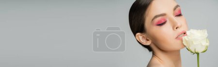 Photo for Sensual woman with pink visage posing with closed eyes near fresh rose isolated on grey, banner - Royalty Free Image
