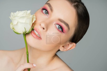 Téléchargez les photos : Portrait de femme charmante posant avec rose blanche visage presque parfait isolé sur gris - en image libre de droit
