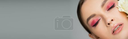 Photo for Portrait of pretty woman with pink visage and fresh rose near face isolated on grey, banner - Royalty Free Image