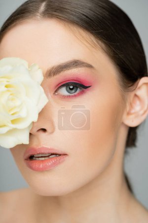 Foto de Primer plano retrato de mujer joven con rostro oscurecido de color rosa con rosa de marfil aislado en gris - Imagen libre de derechos