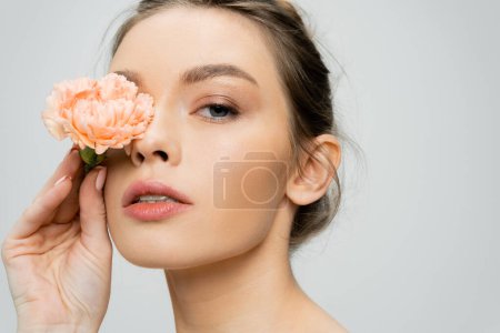 Porträt einer jungen Frau mit perfekter Hautbedeckung Auge mit Nelkenblüte isoliert auf grau