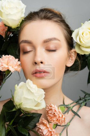 Photo for Portrait of pretty woman with closed eyes and natural makeup near roses and carnations isolated on grey - Royalty Free Image