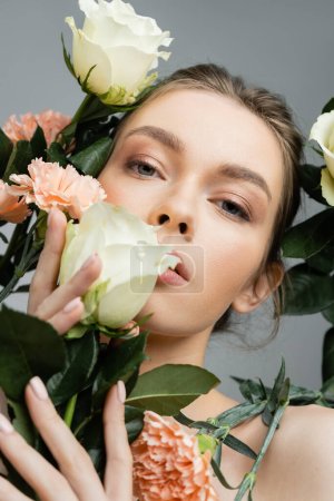 Photo for Sensual woman with perfect face looking at camera while touching fresh flowers isolated on grey - Royalty Free Image