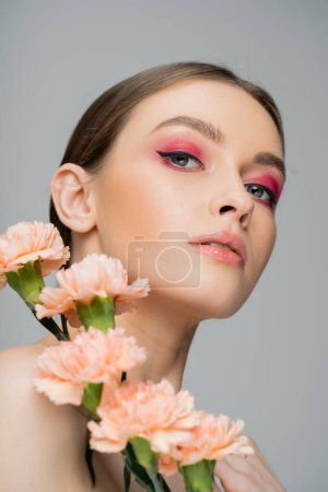Téléchargez les photos : Portrait of young woman with perfect skin and makeup looking at camera near fresh flowers isolated on grey - en image libre de droit