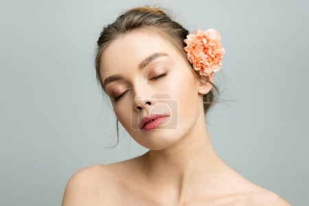Porträt einer charmanten Frau mit geschlossenen Augen und frischer Nelkenblüte hinter dem Ohr isoliert auf grau