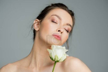 Photo for Young woman with natural makeup and naked shoulders posing with closed eyes near white rose isolated on grey - Royalty Free Image