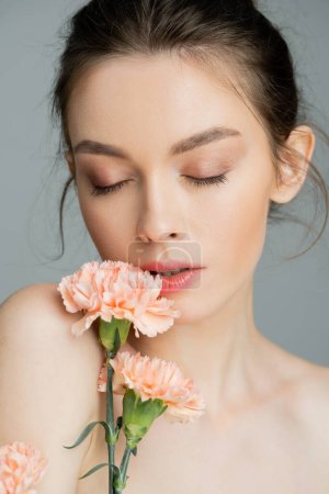 Photo for Portrait of sensual woman posing with closed eyes near peach carnations isolated on grey - Royalty Free Image