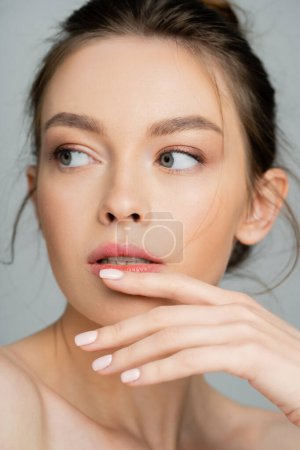 Photo for Portrait of young woman with natural makeup holding hand near chin and looking away isolated on grey - Royalty Free Image