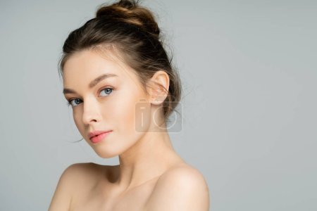 junge Frau mit natürlichem Make-up blickt in Kamera isoliert auf grau 