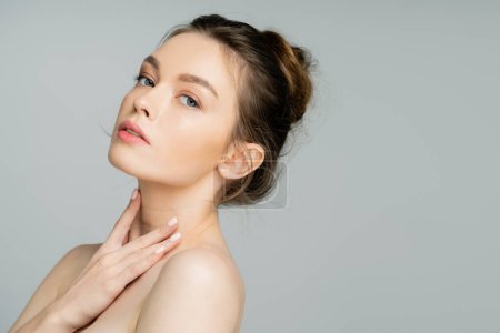 Pretty woman with perfect skin touching neck isolated on grey 