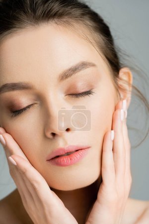 Close up view of young model touching perfect skin isolated on grey 