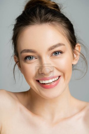 Smiling model with naked shoulders looking at camera isolated on grey 