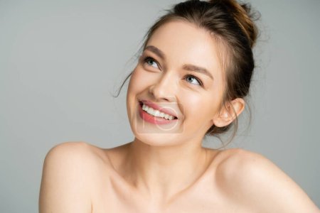 Happy young model with naked shoulders looking up isolated on grey 