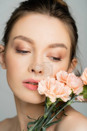 Portrait of woman with natural makeup posing with carnations isolated on grey 