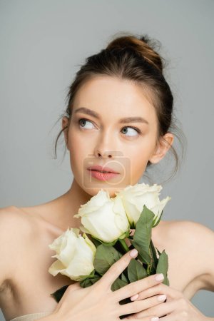 Young woman with naked shoulders holding white roses isolated on grey 
