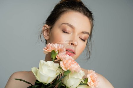 Young woman with natural makeup holding flowers isolated on grey 
