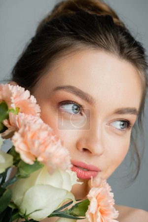 Portrait of pretty young woman looking away near flowers isolated on grey 