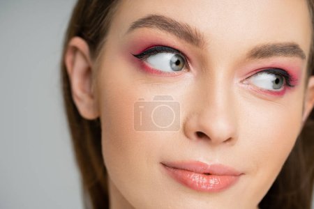 Close up view of young fair haired woman with pink eye shadow isolated on grey 