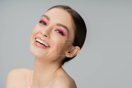 Téléchargez les photos : Cheerful woman with naked shoulders and and bright pink makeup looking at camera isolated on grey - en image libre de droit